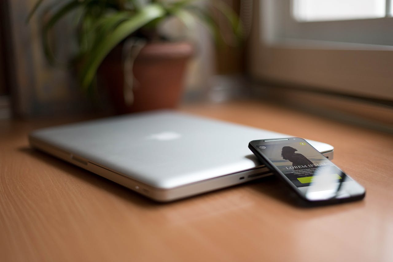 Close-up of a silver laptop and smartphone on a wooden desk, capturing modern work essentials.
